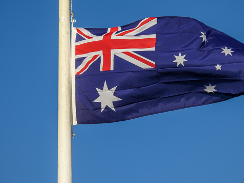 The Australian flag flies at half-mast on a flagpole on Bondi Surf Bathers Life Saving Club on the waterfront at Bondi Beach, Sydney.  This image was taken on a late sunny afternoon at Bondi Beach on 20 October 2023.