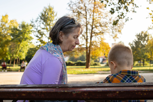 Senior woman with gray hair and her small grandson sitting in park