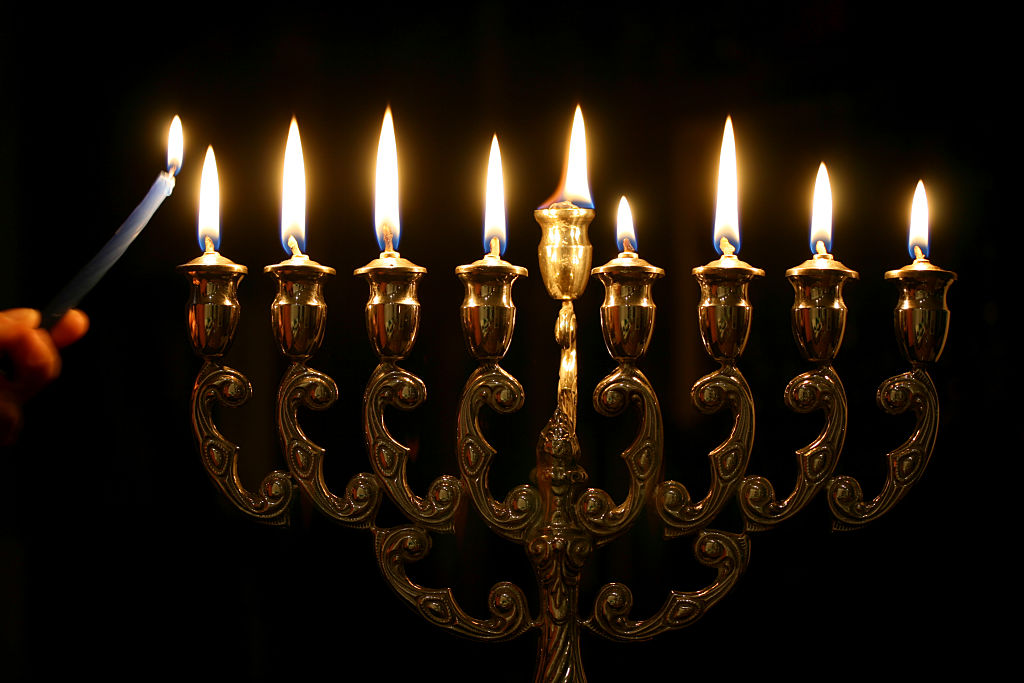 Lighting the menorah. Hand holding candle has motion blur.