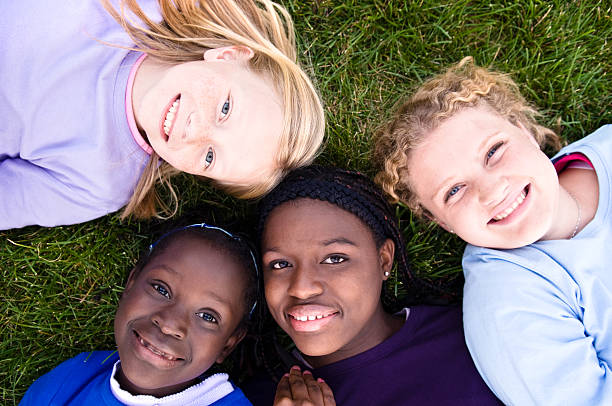 четыре счастливые девочки, лежа на траве - adoption family multi ethnic group human teeth стоковые фото и изображения