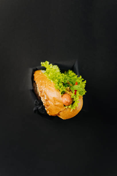 frischer hot dog ragt durch gerissene löcher im papierhintergrund heraus. streetfood-konzept - sausage grilled isolated single object stock-fotos und bilder
