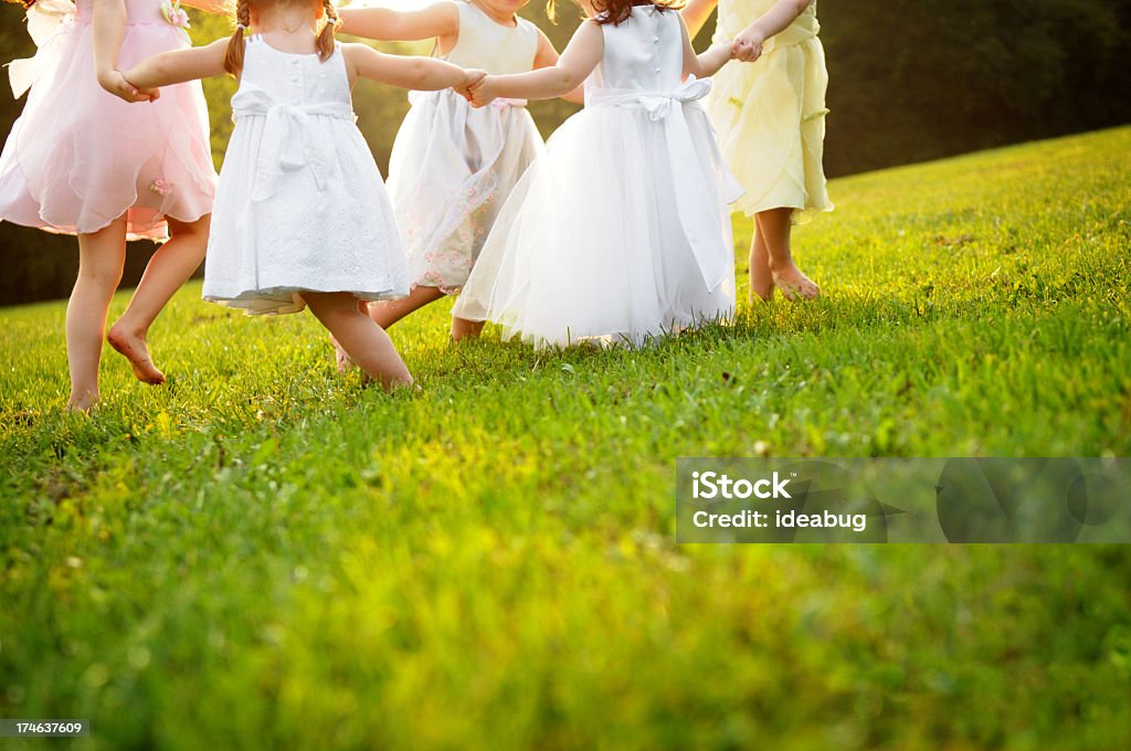 Happy, Little Dancing Princess Girls in Dresses Color photo of five happy little girls wearing princess dresses and dancing in the grass in the evening sun together. Child Stock Photo