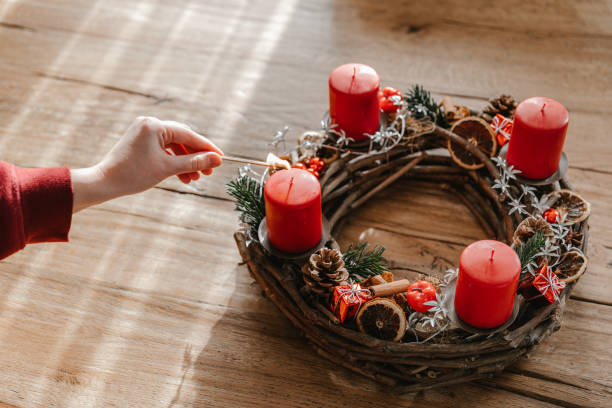 Advent wreath made with branches with four candles lit every sunday before christmas. Advent wreath made with branches with four candles lit every sunday before christmas. Human hand holding a matchstick. advent candle wreath adventskranz stock pictures, royalty-free photos & images
