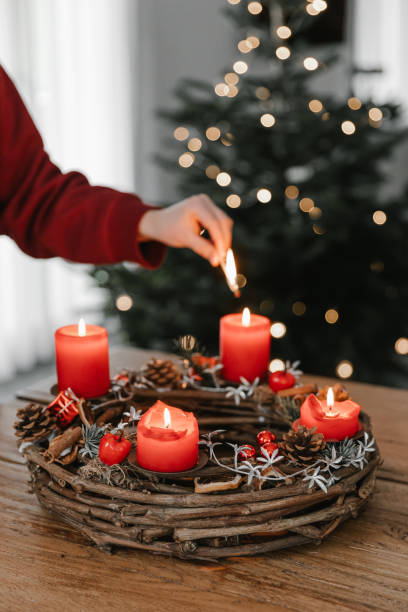 Female hand lighting all four candles on advent wreath on Christmas Eve. Female hand lighting all four candles on advent wreath on Christmas Eve. Celebrating cozy winter time at home. advent candle wreath adventskranz stock pictures, royalty-free photos & images