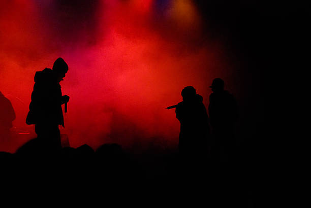 silhouettes of rappers on stage hip hop concert with rapper on stage. red enlightened fog in the background. silhouette of three rappers. little bit of noise in the fog due to high iso rap stock pictures, royalty-free photos & images