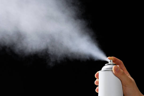 Person spraying an aerosol can against a black background stock photo