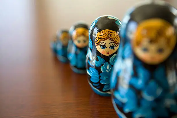 Russian style Matryoshka dolls that stand side by side on a wooden surface. Dolls designed to pull in half and fit perfectly inside the larger.