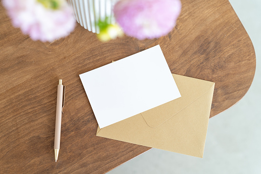 Blank sheet of paper on brown envelope, pen on the desk. Greeting, wedding or congratulations stationery mockup