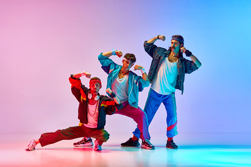 Funny image of three men in stylish, vintage sportswear training aerobics and gymnastics against gradient pink blue background in neon light. Concept of sportive and active lifestyle, retro style. Ad
