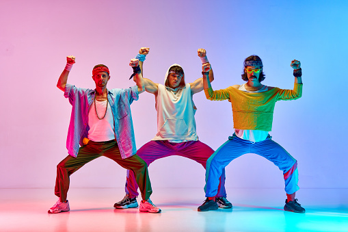 Warming-up. Men in colorful, stylish, vintage sportswear training against gradient pink blue background in neon light. Concept of sportive and active lifestyle, humor, retro style. Ad
