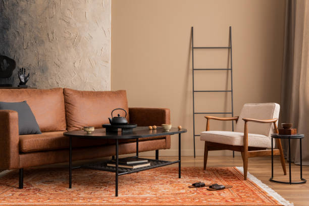 istock Warm and cozy living room interior with mock up poster frame, brown sofa, black coffee table, patterned rug, boucle armchair, pillows and personal accessories. Home decor. Template. 1746451817