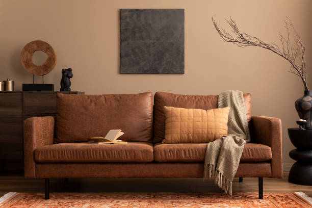 istock Warm and cozy living room interior with mock up poster frame, brown sofa, black coffee table, ladder, patterned rug and personal accessories. Home decor. Template. 1746452366