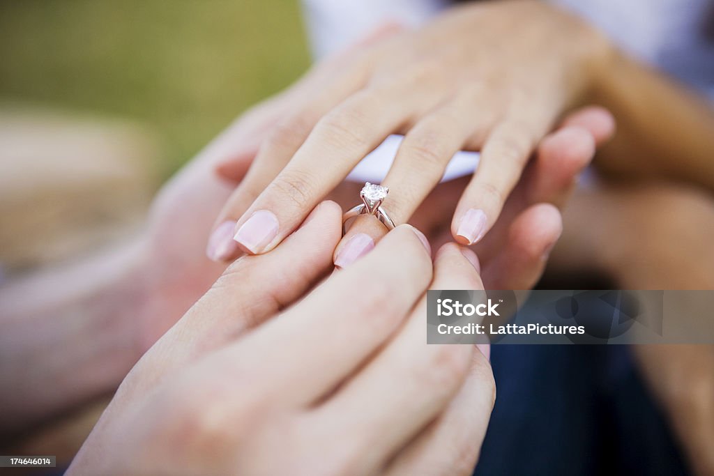 Female and male hands slipping on engagment ring Young man is seen slipping an engagement ring on his girlfriend's ring finger. Engagement Ring Stock Photo