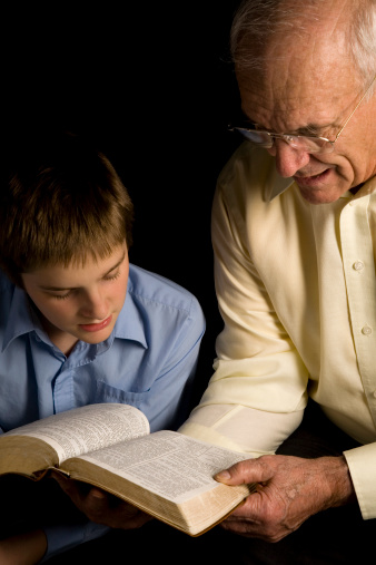 A grandfather reads from the Bible to his grandson.