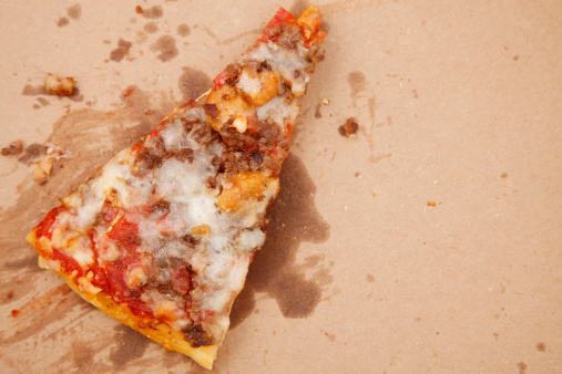 A greasy slice of pizza in a grease stained cardboard box.