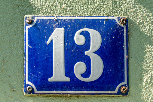Number 13 is considered an unlucky number in many countries. Old-fashioned enamel sign on a green house wall.