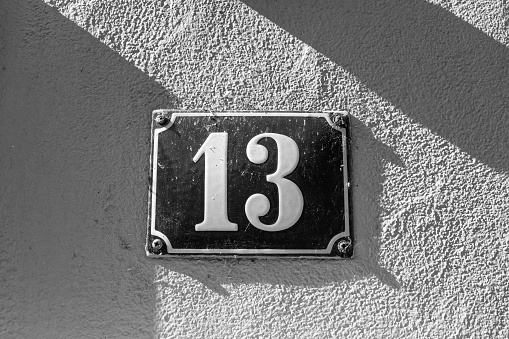 Number 13 is considered an unlucky number in many countries. Old-fashioned enamel sign on a house wall. B&W.