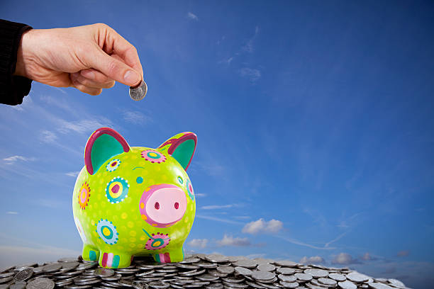 Hand Dropping Coin into Multi Coloured Savings Piggy Bank stock photo