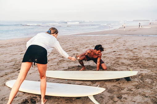 young couple kneeling on sandy beach and waxing their surfboard on the beach