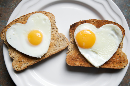 Romantic breakfast with heart shaped fried egg and toasts on white wooden table, flat lay. Space for text