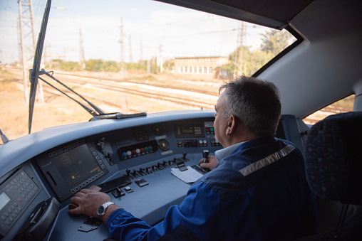 Adult male in a locomotive instrument panel room, cockpit. Train engineer driving the train