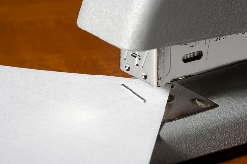 Close-up shot of a stapler and 3 pages of paper stapled together.