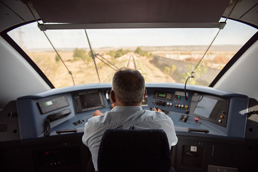 Train engineer, driving the locomotive from the instrument control room, cockpit. Railroad visible