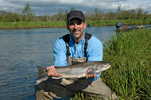 Smiling middle aged fisherman and his salmon in Alaska