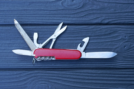 one open folding knive multitools with red handles with gray blades lies on a black wooden table