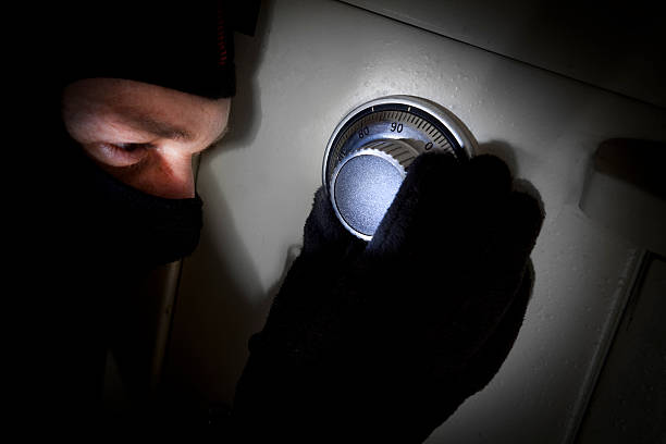 Safe Cracking Balaclava Clad Cat Burglar Burglar wearing balaclava and gloves attempts to crack a torch lit combination lock on a safe. clad stock pictures, royalty-free photos & images