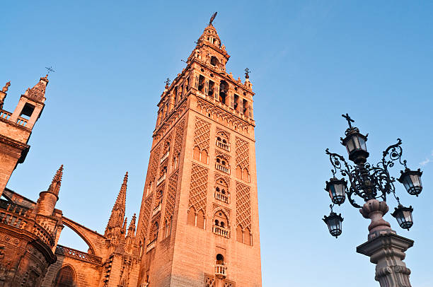 The Giralda Seville Cathedral dawn glow "Warm early morning light of daybreak illuminating the iconic Moorish and Renaissance bell tower of La Giralda and the ornate gothic facade of the Catedral above the Plaza Virgen de los Reyes in the picturesque Santa Cruz district of Seville, Andalusia, Spain. ProPhoto RGB profile for maximum color fidelity and gamut." seville photos stock pictures, royalty-free photos & images
