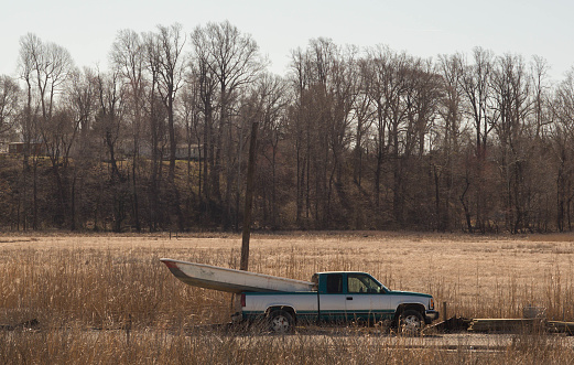 A small boat rests in the back of a green and silver pickup truck near a field.