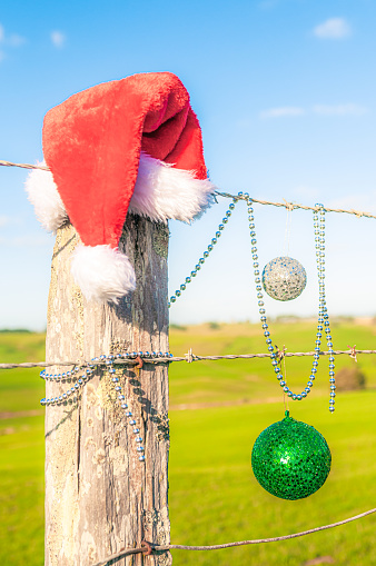Close-up of Christmas decorations, with a Santa hat on a fencepost, in a warm summer breeze on a farm in the Southern Hemisphere.