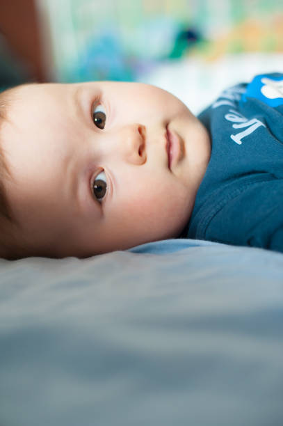 ritratto di bambino sveglio sdraiato sul letto e guardando la macchina fotografica - playground cute baby blue foto e immagini stock