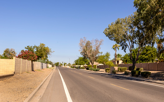 Narrow unmarked designated bike lane separated from main road part by a wide white line along North 37th Avenue in residential area on North-West Phoenix, Arizona; copy space