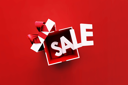 The sale word coming out of a  white gift box tied with red ribbon on red background. Horizontal composition with copy space. Directly above. Great use for sale concepts.