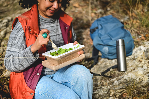 Woman with backpack and thermos resting on on the ground in the forest.