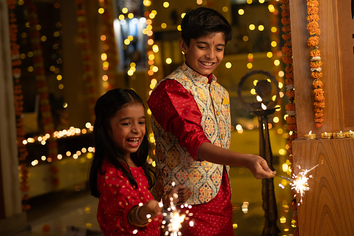 Smiling boy with girl burning sparkler while standing in illuminated home during Diwali festival