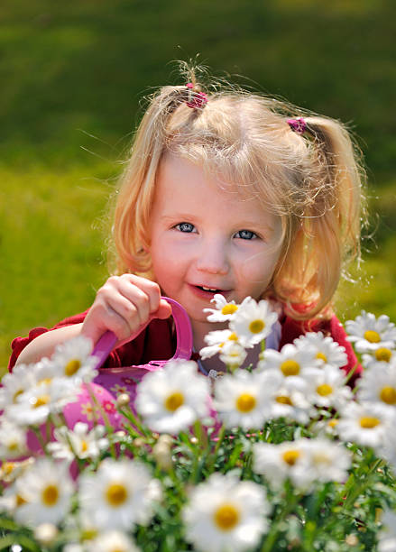 Portrait of 5 years old girl posing in front of yellow daisy flowers. She is wearing a striped blue dress. Shot under daylight with a full frame mirrorless camera.