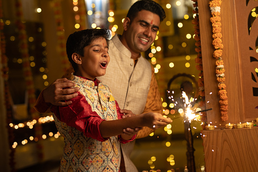 Happy father and son burning sparklers while celebrating Diwali festival together at illuminated apartment