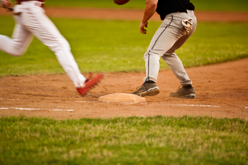 Low angle selective focus view of a baseball in grass with outfield fence in the background