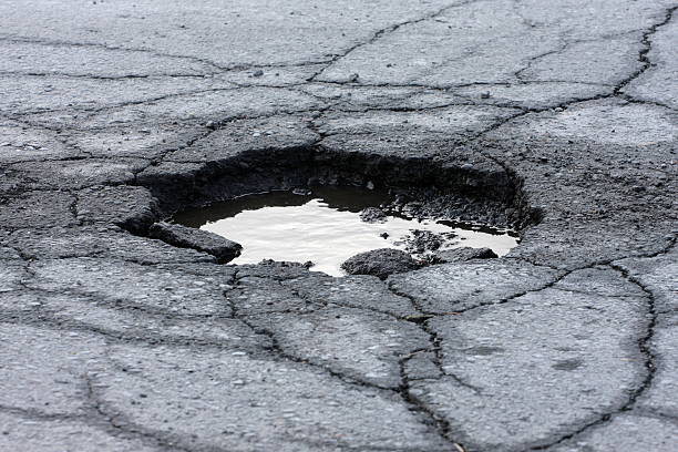 Pot Hole "Broken asphalt pavement resulting in a pothole, dangerous to motorists. Shot with shallow dof.  ....recent addition" sinkhole stock pictures, royalty-free photos & images
