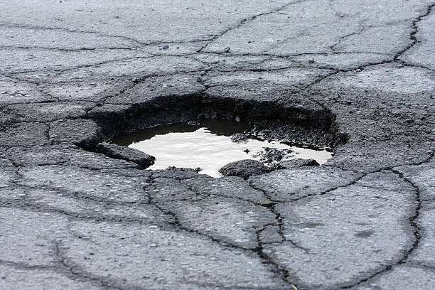 Pot Hole "Broken asphalt pavement resulting in a pothole, dangerous to motorists. Shot with shallow dof. ....recent addition" sinkhole stock pictures, royalty-free photos & images