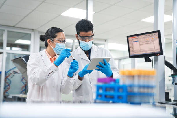 istock Female and male biochemists wearing protective face masks while discussing over digital tablet at laboratory 1746635126