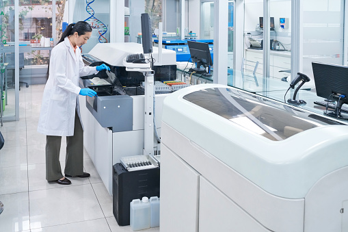 Full length of female technician examining machinery at science lab