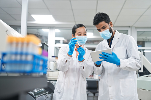 Male and female scientists wearing protective face masks while discussing over digital tablet at laboratory