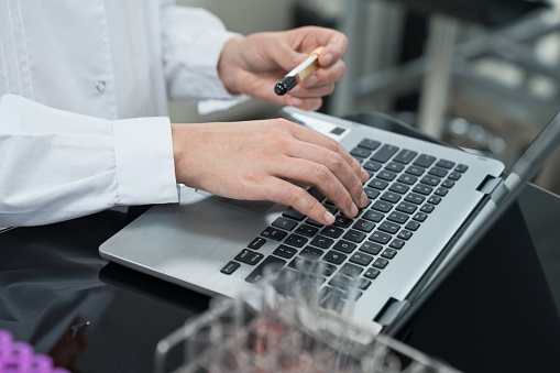 Midsection of female scientist holding sample while using laptop at laboratory