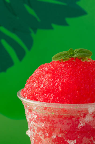 istock A strawberry and cherry red fruit flavored shaved ice or slush with lemon in a clear disposable cup on a green paper background decorated with green paper leaves. 1746640247