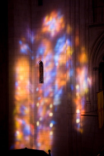 Colorful and muted stained glass window reflections of morning light on a wall of the National Cathedral.
