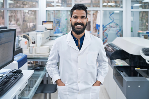 Portrait of smiling young male biochemist standing with hands in pockets at laboratory